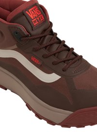 Brązowe botki Vans z teksturową cholewką, prezentujące biały wzór fali, czerwone akcenty oraz wytrzymałą podeszwę zapewniającą przyczepność.