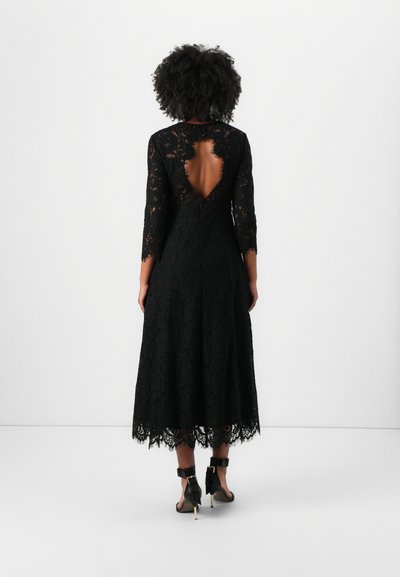 Robe noire en dentelle avec des manches longues, dos nu et ourlet festonné. Design longue jusqu'au sol avec un motif floral complexe et une taille cintrée.