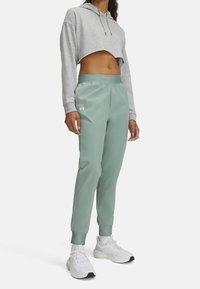 Kort grå hoodie med snörning, kombinerad med ljusgröna sportiga joggerbyxor med elastisk midja och ribbade muddar. Vita sneakers.