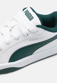 Baskets en cuir blanc avec accents verts, présentant des bandes texturées sur les côtés, des lacets épais blancs et un col rembourré pour le confort.