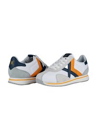 Zapatillas de malla blanca con detalles de ante gris, superposiciones en azul marino y naranja, cordones blancos y una suela texturizada. Presenta un logo en el talón.