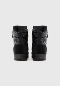 Une paire de bottes d'hiver noires isolées avec des semelles épaisses et des tirants, vues de l'arrière sur un fond blanc.