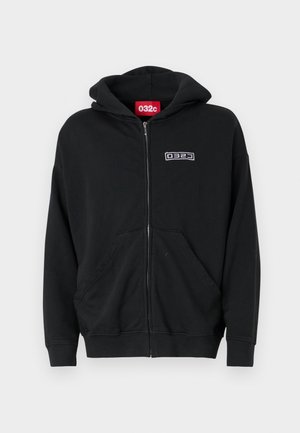 Black zip-up hoodie with front pockets, small white "032c" logo on left chest, and red label inside the collar.