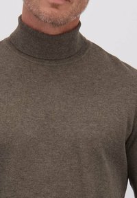 Donkere olijfgroene coltrui gemaakt van zacht gebreid materiaal, met een subtiel logo op de borst en een aansluitende pasvorm.