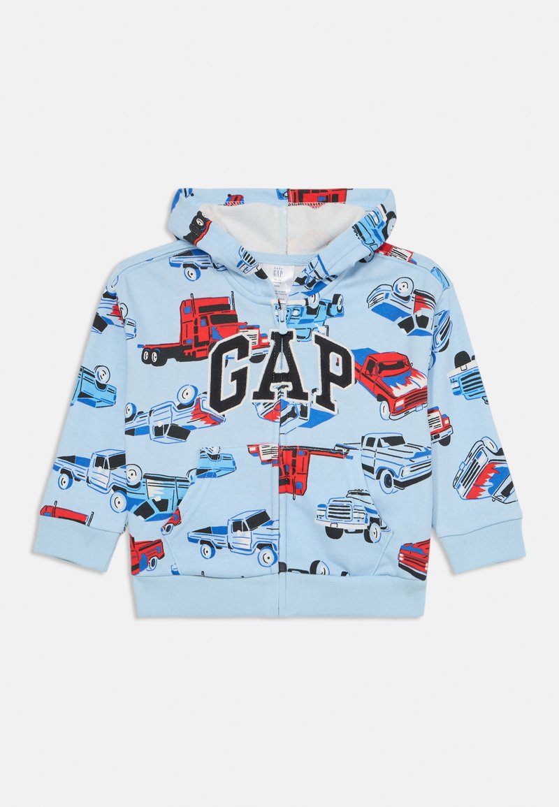 Felpa blu chiaro con un motivo di camion in rosso e nero. Chiusura frontale con zip e grande logo "GAP". Tessuto morbido e polsini elasticizzati.