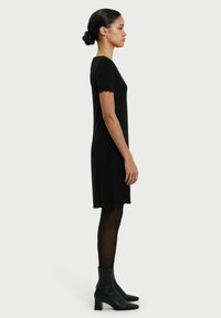 Zwart geribbelde jurk met korte mouwen, jurk tot op de knie, textuurstof, gecombineerd met zwarte enkellaarsjes en panty’s, zijaanzicht.