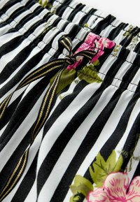 Tessuto a righe bianche e nere con stampa floreale rosa e un nastro nero con strisce dorate annodato a fiocco su una cintura elastica.