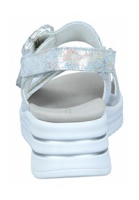 White sandals with shimmering iridescent straps, cushioned footbed, and a thick, textured white sole featuring silver accents.