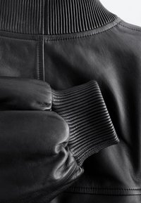 Manche de veste en cuir noir avec poignets en maille côtelée et col en maille côtelée visibles sur un panneau arrière en cuir lisse.