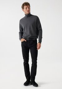 Sivi pulover s rolkragnom uparen s crnim skinny trapericama. Pulover ima duge rukave i glatku teksturu. Model nosi crne čizme do gležnja.