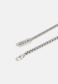 Bracelet en chaîne argentée avec une étiquette rectangulaire plate gravée avec "ICON" et un fermoir à lobster pour une fermeture sécurisée.