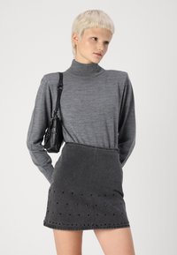 Siv turtleneck pulover z dolgimi rokavi, uparen z črno jeans krilo, ki ima okrasne kovinske dodatke na robu. Majhna črna torbica nošena čez ramo.