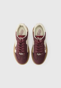 Baskets bordeaux avec un dessus crème, dotées d'une semelle en caoutchouc, de lacets et d'un détail de logo. Texture en cuir lisse et design sportif classique.