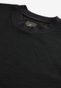 Schwarzer Sweatshirt mit einem strukturierten Rautenmuster, geripptem Halsausschnitt und einem Etikett mit der Aufschrift "NEXT". Das Material wirkt weich und dick.