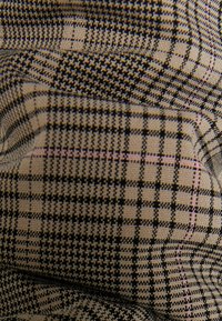 Tkanina z czarno-beżowym wzorem w kratkę, z drobnymi, kontrastującymi liniami i subtelnymi różowymi akcentami, ukazująca skomplikowany splot i fakturę.