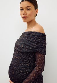 Robe décolletée en tissu noir transparent à imprimé léopard marron. Présente des fronces sur le corsage et les manches, une silhouette cintrée mettant en valeur la taille.
