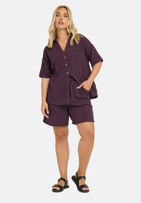 Lila puuvillane lühikeste varrukatega nööbiga särk, millel on tasku, koos sobivate lühikesed pükstega. Mudel kannab musti sandaale. Lihtne, mugav lõige.