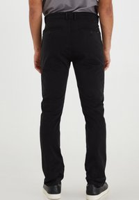 Černé kalhoty vyrobené z bavlněné směsi, slim fit design, dvě zadní kapsy s knoflíky a hladká textura, nošené s černými teniskami.