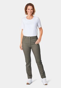 Lichte witte shirt met korte mouwen gecombineerd met olijfgroene, getailleerde broek en witte sneakers; heeft een ronde halslijn en een knoopsluiting bij de taille.