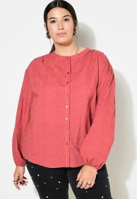 Camicia rossa realizzata in tessuto testurizzato, con scollatura rotonda, chiusura con bottoni e maniche lunghe a palloncino. Design semplice senza fantasie.