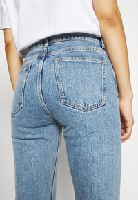 Jean en denim bleu clair à taille haute, avec des coutures contrastées et deux poches arrière. La texture semble douce avec une finition légèrement délavée.