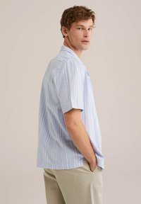 Chemise à manches courtes avec boutonnière en bleu clair à rayures verticales blanches. Dispose d'un col, d'une poche poitrine et d'une coupe décontractée. Le tissu semble léger.