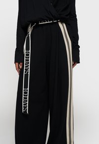 Losse zwarte broek met een brede tailleband. Beschikt over een crèmekleurige "TODAYS" logo-riem en zijstrepen. Zachte stof, ontspannen silhouet.