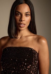 Sort stropløs top med paljetter og en glat tekstur. Den har en tætsiddende silhuet og reflekterer lys med paljetter i en rosaguldfarve.