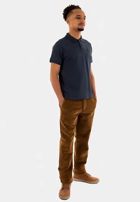 Mörkblå pikétröja med korta ärmar, kombinerad med bruna manchesterbyxor och ljusbruna skor. Enkel, klassisk design med ledig passform.