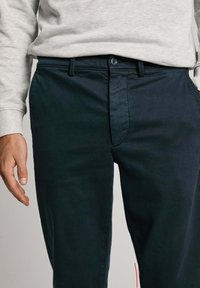 Dark blue chinos with a smooth texture, featuring front pockets, a button closure, and a zip fly. The fabric appears durable and lightweight.