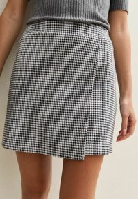 Close-up van een persoon die een zwart-wit houndstooth minirok en een ribbelgrijze top draagt, waarbij de taille en de bovenbenen zichtbaar zijn.