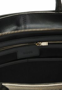 Interno di una borsa a tracolla nera in pelle con cerniera dorata e etichetta del marchio. Presenta un ampio scomparto con foderatura nera e più tasche.