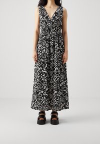 Robe longue avec un motif floral abstrait noir et blanc, décolleté en V, sans manches, taille cintrée et silhouette évasée en ligne A.