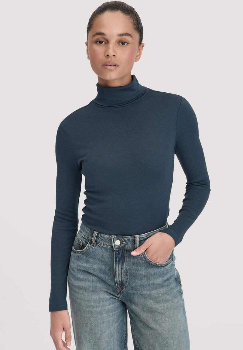 Marineblaues Rollkragenshirt aus elastischem Material, mit langen Ärmeln und taillierter Passform, kombiniert mit hellblauen, hoch geschnittenen Jeans.