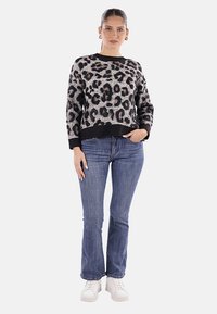Maglione a stampa leopardata in morbido tessuto con polsini e orlo a coste neri, abbinato a jeans a zampa blu e sneakers bianche.