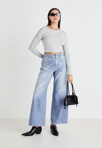 Siv majica s dolgimi rokavi, svetlo modri široki jeans hlače, črni čevlji z ostrim sprednjem delom in mala črna torbica. Gladke teksture in preprost dizajn.