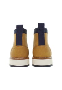 Stivali in pelle marrone con linguette in tessuto nero, colletto imbottito nero, suole bianche e battistrada nero, visti da dietro su uno sfondo bianco.