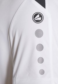 Maglietta sportiva bianca con un logo rotondo e quattro accenti a pois neri sulla spalla sinistra. Realizzata in tessuto morbido e leggero.