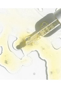 Genomskinlig pipettflaska med gyllene vätska, texturerade bubblor och ljusreflektioner på en ljus bakgrund. Innehåller ett trögflytande oljeliknande ämne.