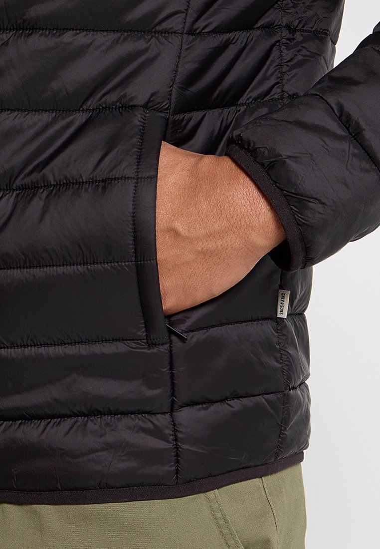 Giacca a vento nera con texture trapuntata, dotata di tasca laterale e polsini elasticizzati. Tessuto leggero e liscio con un design aderente.