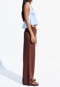 Jasnoniebieski, halterowy crop top z fasonem peplum, połączony z luźnymi, brązowymi spodniami na sznurku i czarnymi sandałami. Gładka faktura materiału.