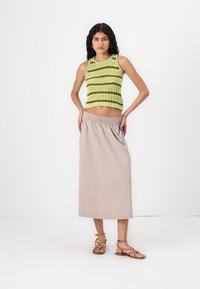 Débardeur en tricot vert vif avec des rayures jaunes, associé à une jupe maxi beige unie et des sandales à lanières brunes. Textures lisses tout au long.