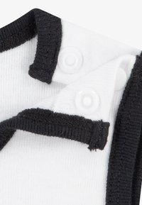 Hvit bomullsstoff med svart kragedetalj, har to trykknapper og en teksturert strikk, viser en nærbilde av halslinjens design.
