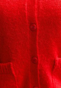 Röd cardigan med ett mjukt, strukturerat stickat mönster. Har fyra matchande röda knappar och två framfickor. Det enkla designen ökar värmen och komforten.
