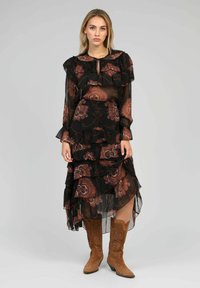 Robe noire avec tissu transparent, couches volantées et motifs floraux en marron et orange. Associée à des bottes de style western marron.