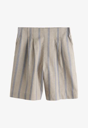 Donna che indossa un gilet senza maniche beige e blu a righe e pantaloncini ampi abbinati, in piedi all'interno con le mani nelle tasche.