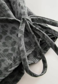 Gray textured fabric with a subtle leopard print pattern, featuring long ties for fastening and a stitched hem detail.