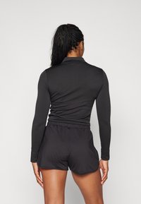 Svart långärmad topp med mockkrage och figursydd design, i kombination med svarta shorts med elastisk midja och en rundad nederkant.