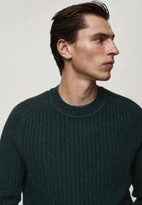 Maglione a coste di un verde scuro con design a girocollo, caratterizzato da un tessuto testurizzato e da dettagli sottili sulle spalle.