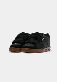Sorte sneakers med en tekstureret overdel, fremtrædende snørebånd, gummisål og brune detaljer. Har perforeret design og logo-detalje på siden.